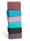 Stack of colorful foam yoga blocks by Everyday Yoga, featuring shades of purple, black, teal, pink, and maroon. Ideal for enhancing flexibility and support during yoga practice, these durable blocks are essential for yogis of all levels.